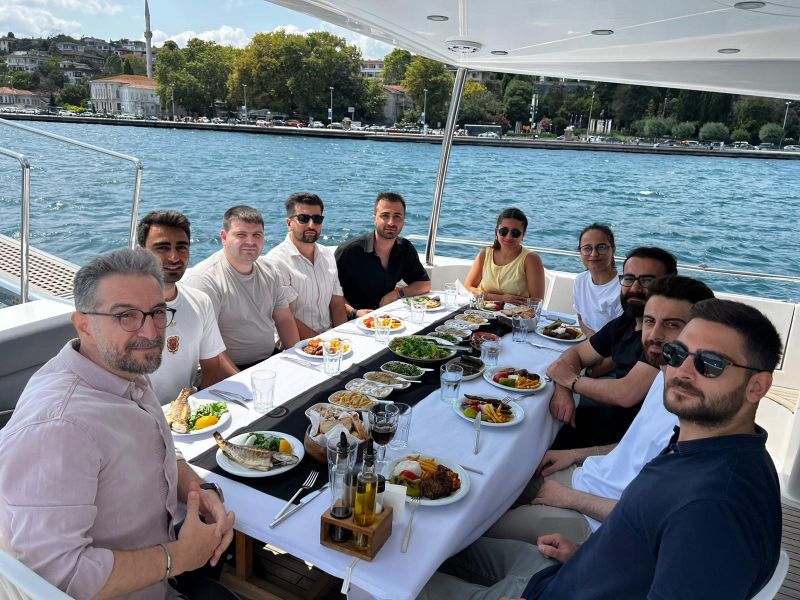 Retmind ekibi teknede, arka planda İstanbul Boğazı, öğle yemeği masasında